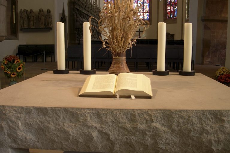 Erdbestattung, Ein Altar in einer Kirche aus Stein, mit einer aufgeklappten Bibel und Kerzen dahinter